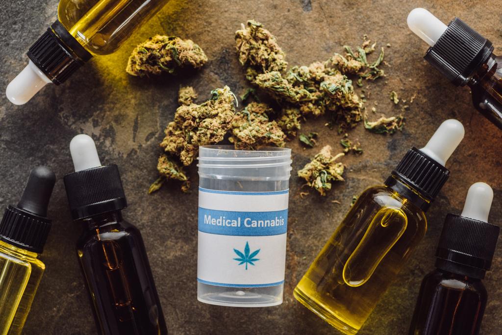 vista dall'alto di germogli di marijuana medica vicino al contenitore e bottiglie con olio di canapa sulla superficie di marmo
 - Foto, immagini