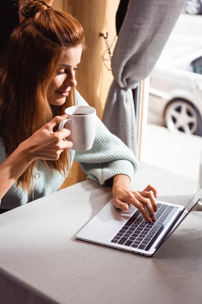 kaunis punapää nainen kupin kahvia kannettavan tietokoneen avulla kahvilassa
 - Valokuva, kuva