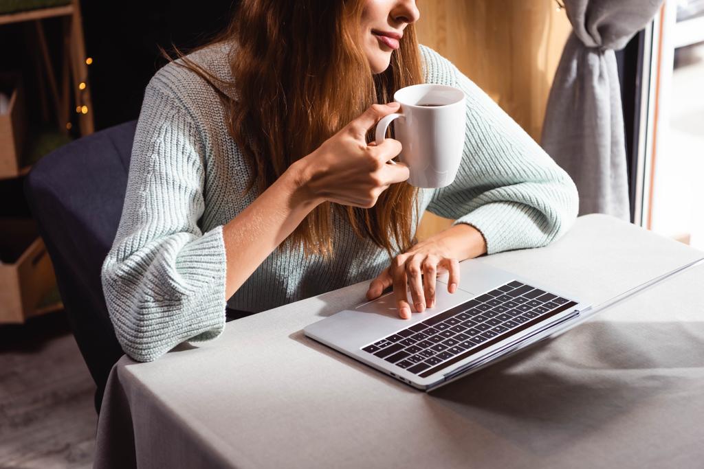 vista recortada de la chica con taza de café usando el ordenador portátil en la cafetería
 - Foto, imagen