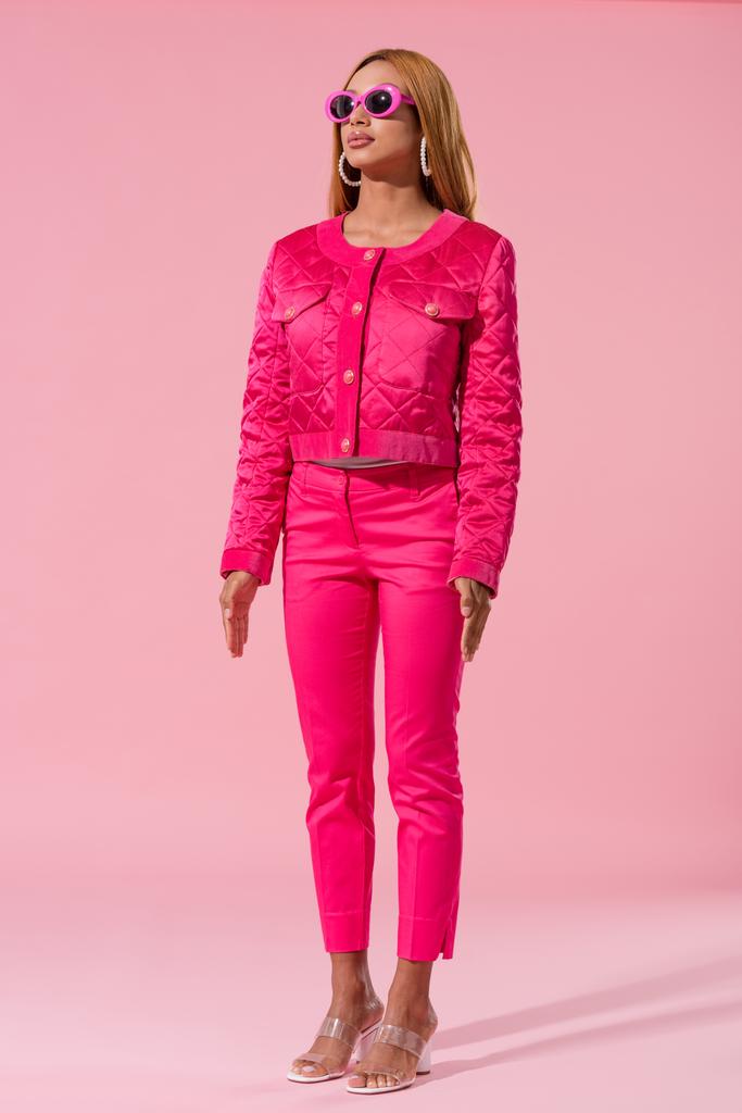 trendy Afrikaans amerikaanse vrouw in zonnebril staan op roze achtergrond, mode pop concept - Foto, afbeelding