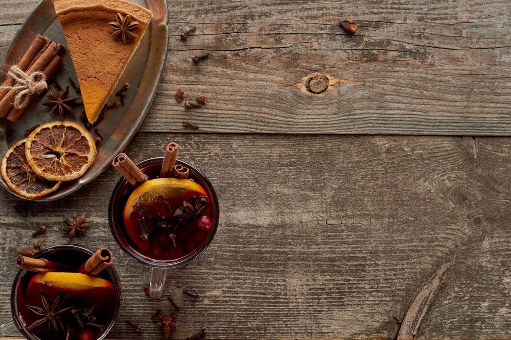 top view of piece of pie and red spiced mulled wine with berries, anise, orange slices and cinnamon on wooden rustic table - Photo, Image