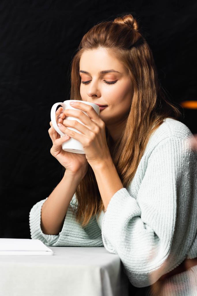 czuła kobieta z zamkniętymi oczami trzymająca filiżankę kawy w kawiarni  - Zdjęcie, obraz