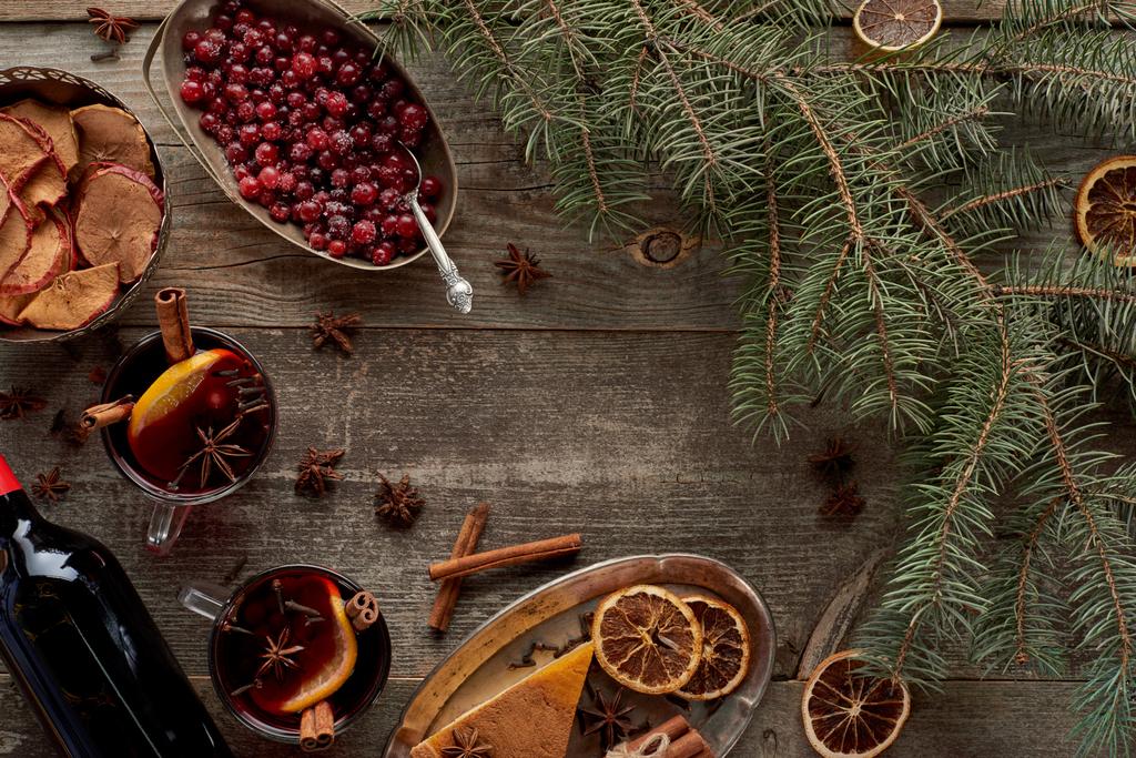 vue du dessus du vin chaud épicé rouge près de la branche de sapin, des baies, de l'anis, des tranches d'orange et de la cannelle sur une table rustique en bois
 - Photo, image