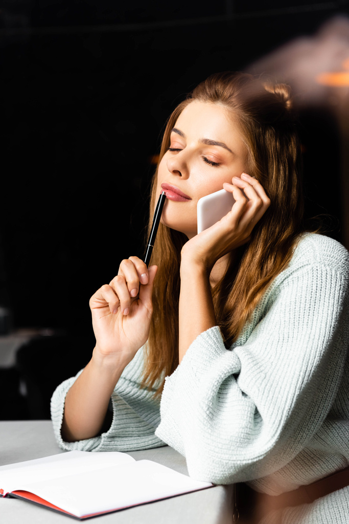 мечтательная женщина с закрытыми глазами разговаривает на смартфоне в кафе с блокнотом
  - Фото, изображение