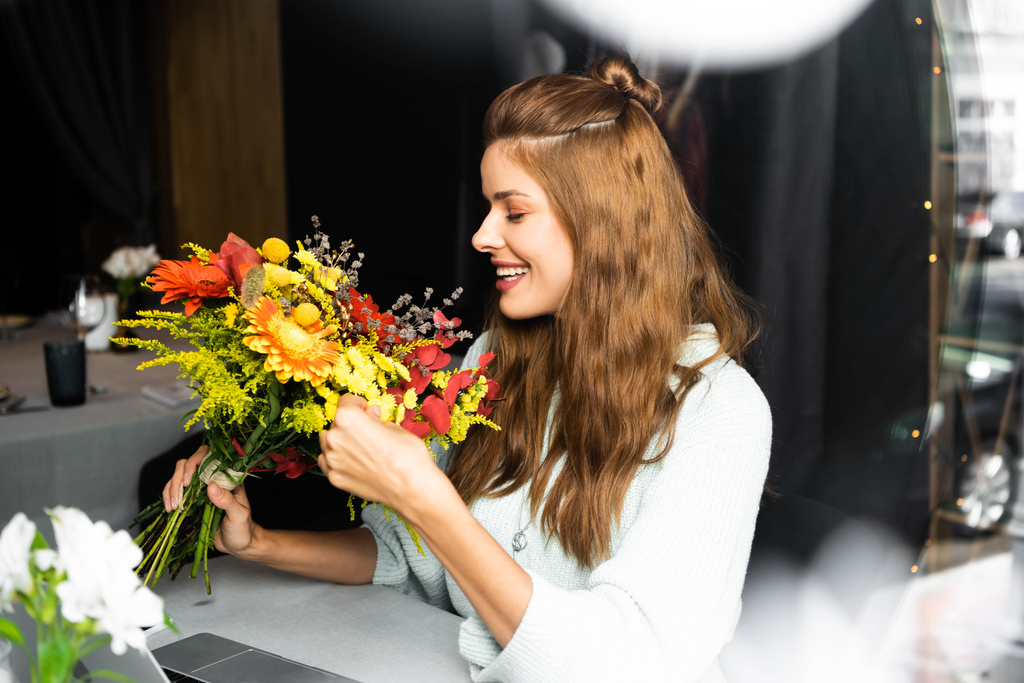 привлекательная улыбающаяся женщина с букетом осенних цветов в кафе
 - Фото, изображение