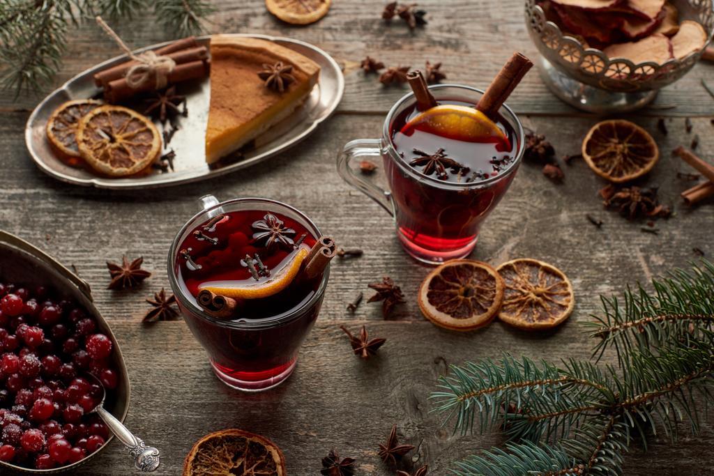vinho quente picado vermelho perto do ramo de abeto, torta, bagas e especiarias na mesa rústica de madeira
 - Foto, Imagem