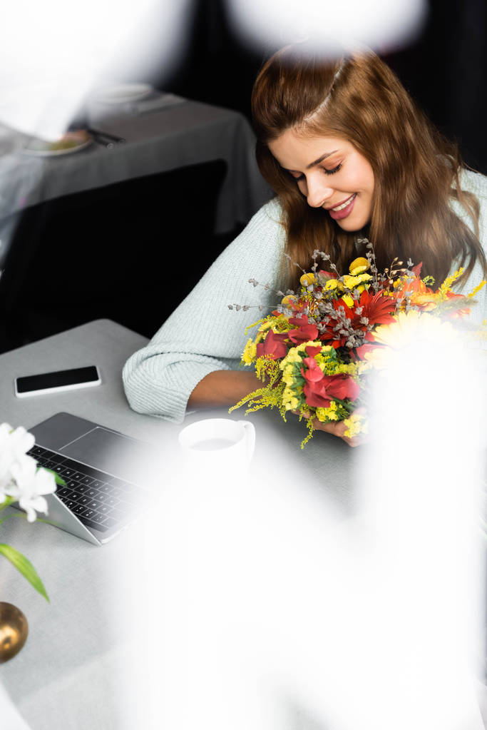 χαρούμενη γυναίκα με μπουκέτο φθινοπωρινά λουλούδια σε καφέ με ψηφιακές συσκευές - Φωτογραφία, εικόνα
