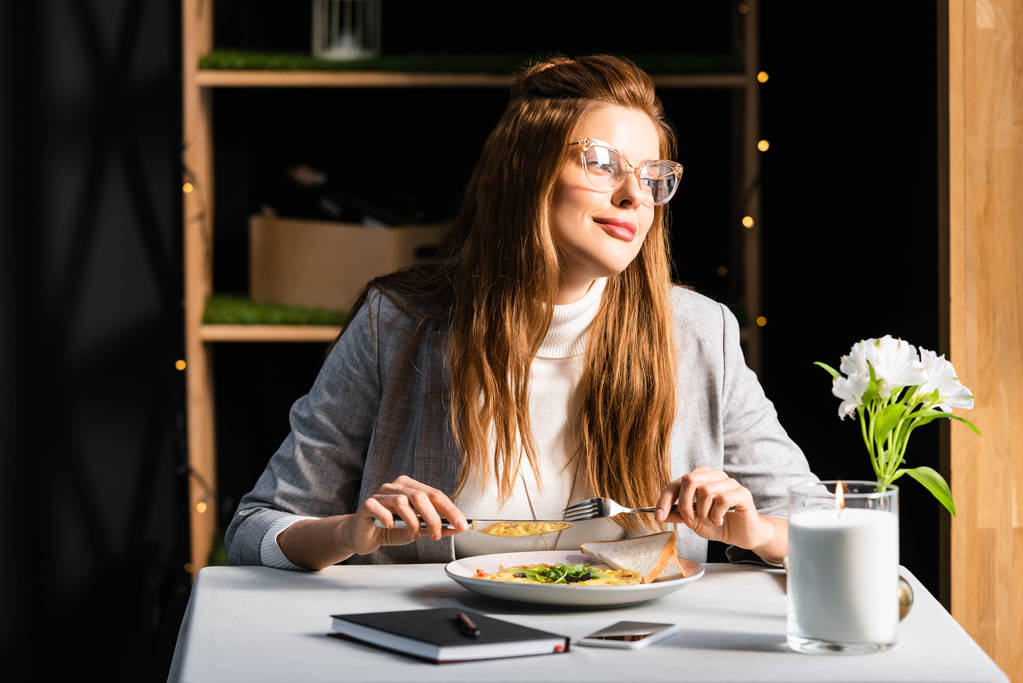 ノートパッドとスマートフォンでカフェで朝食を食べる美しい女性 - 写真・画像