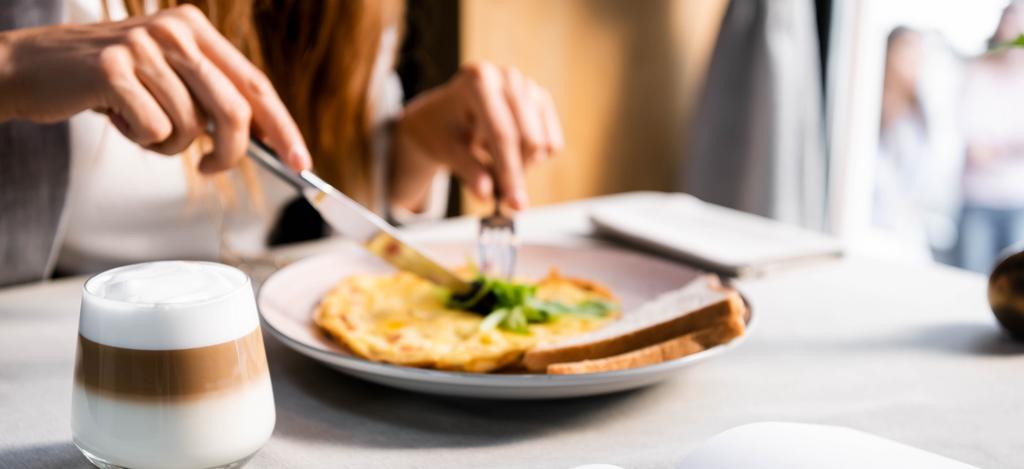 bijgesneden weergave van meisje met omelet en glas koffie voor het ontbijt in cafe  - Foto, afbeelding