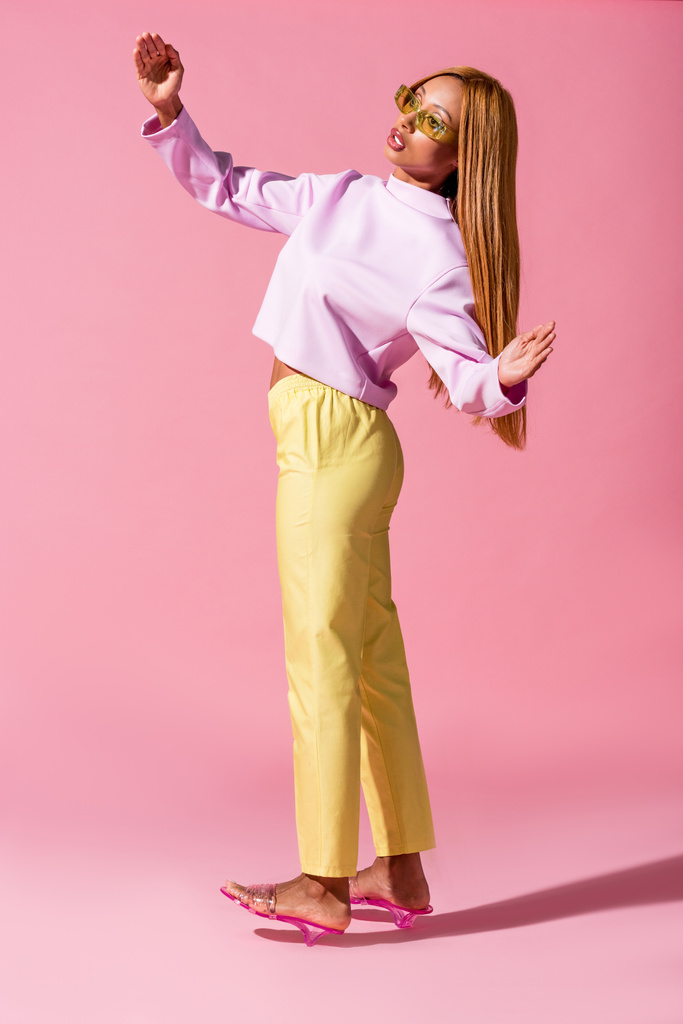 stijlvol Afrikaans amerikaans vrouw staan op roze achtergrond, mode pop concept - Foto, afbeelding