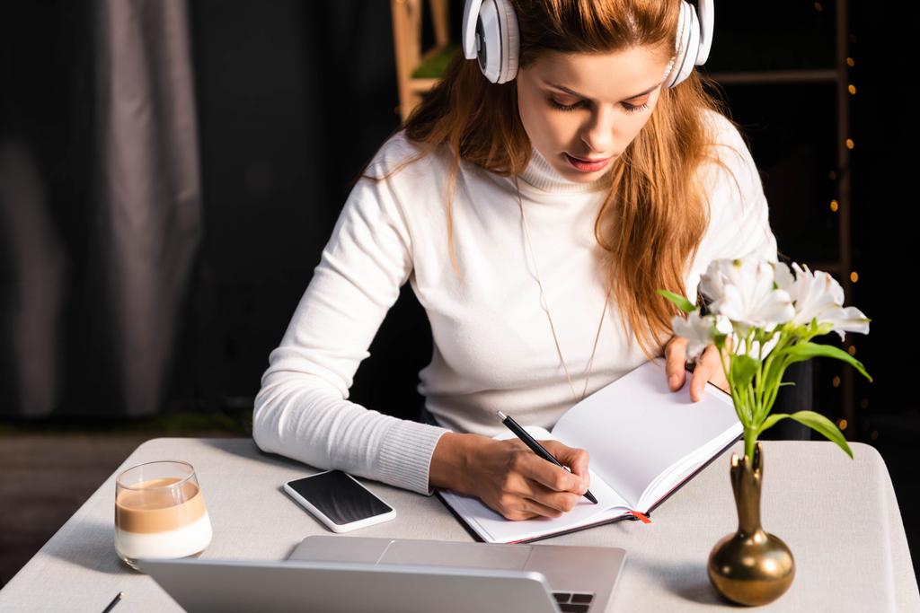 gyönyörű vörös hajú nő fejhallgató nézi webinar laptopon kávézóban - Fotó, kép