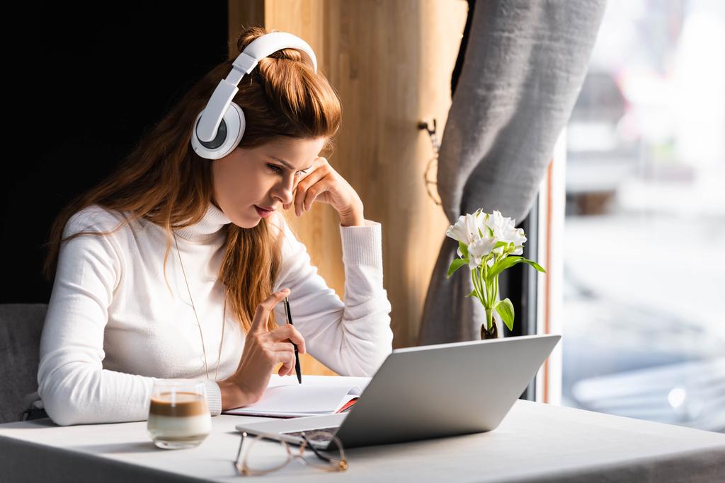 mooie attente vrouw in hoofdtelefoon kijken webinar op laptop in cafe - Foto, afbeelding