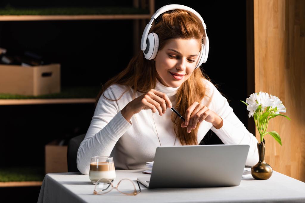 zrzka usmívající se žena ve sluchátkách sledování webinář na notebooku v kavárně - Fotografie, Obrázek