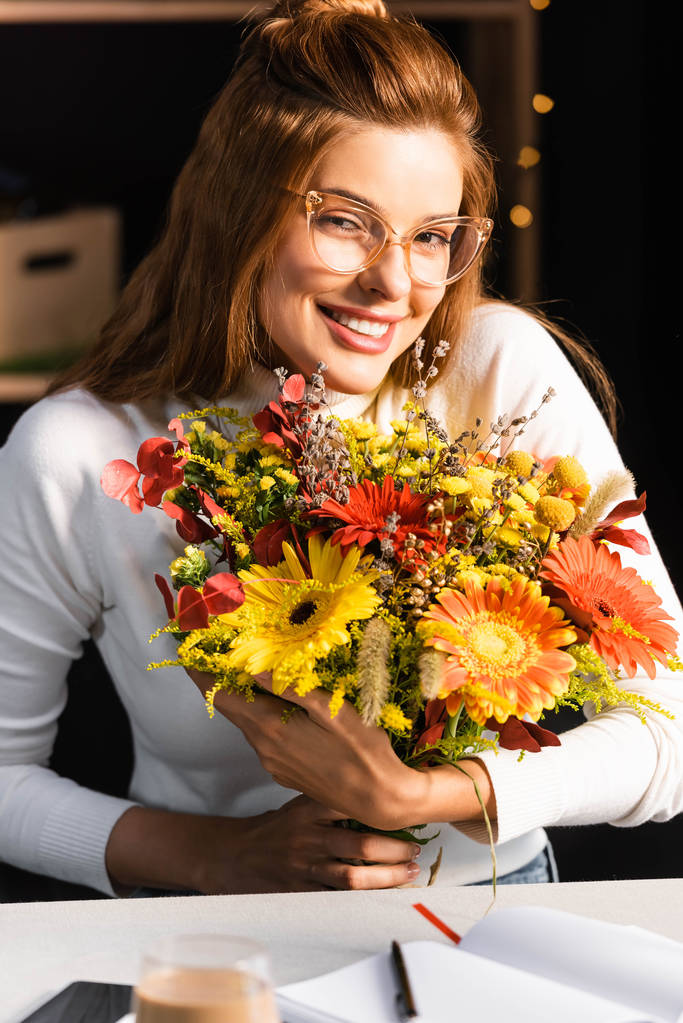 Kahvede elinde bir buket sonbahar çiçeğiyle gülümseyen kadın.  - Fotoğraf, Görsel