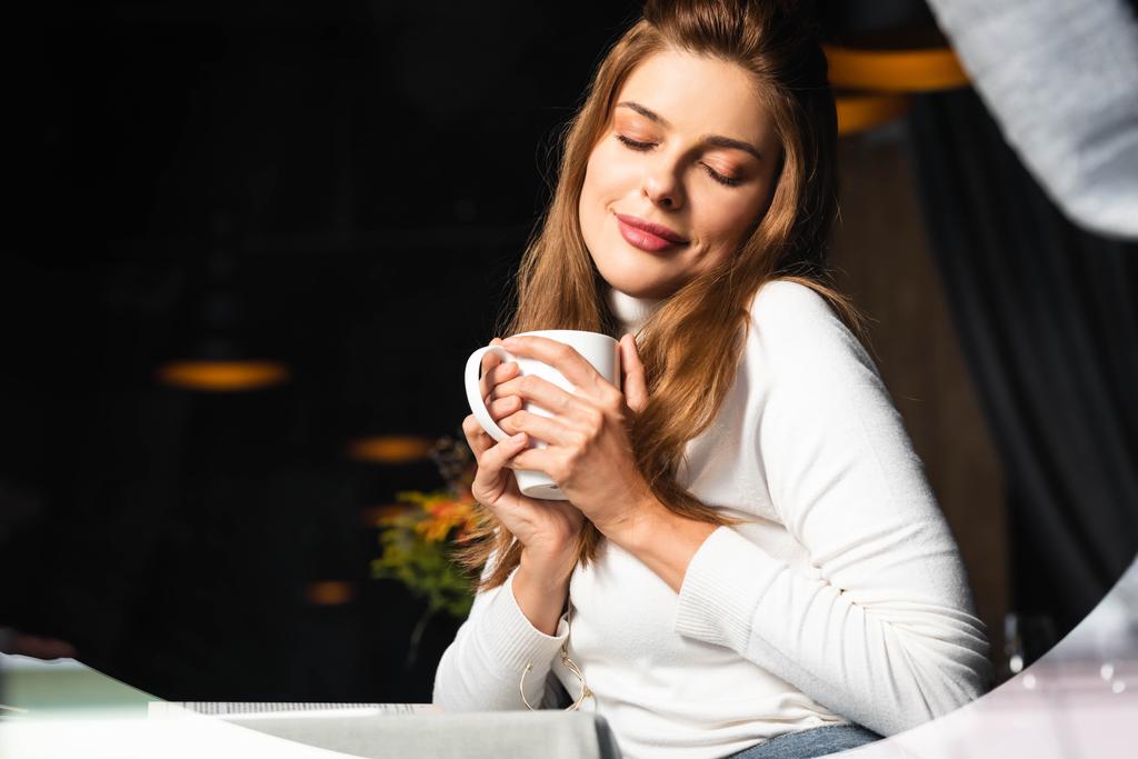 ονειρεμένη γυναίκα με κλειστά μάτια που κρατάει ένα φλιτζάνι καφέ στο καφέ  - Φωτογραφία, εικόνα