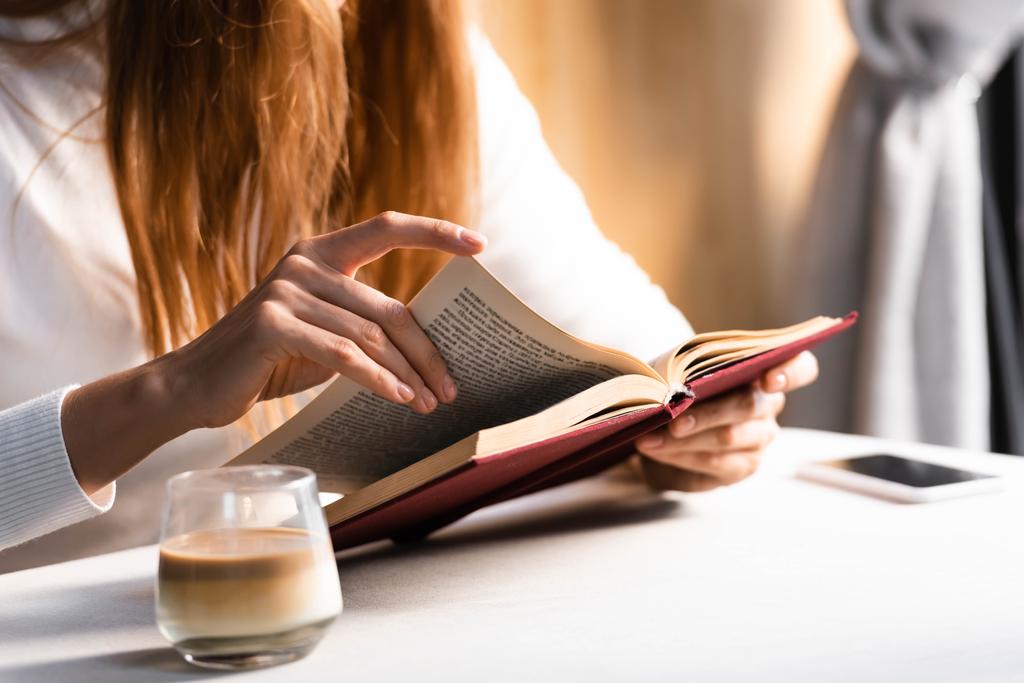 przycięty widok kobiety ze szklanką książki do czytania kawy w kawiarni  - Zdjęcie, obraz