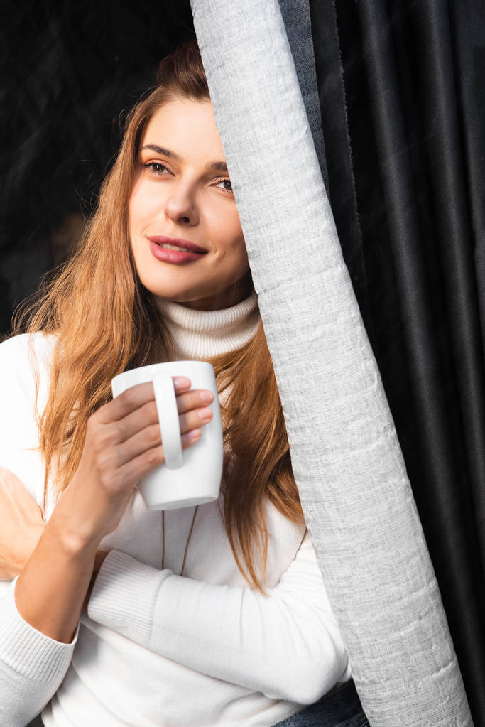 aantrekkelijke vrouw met kopje koffie in cafe in de buurt van venster - Foto, afbeelding