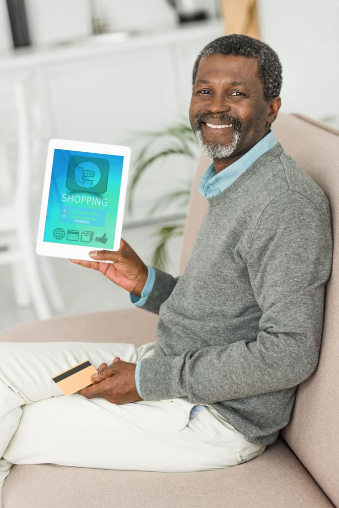 uomo afroamericano sorridente in possesso di carta di credito e mostrando tablet digitale con app di shopping online sullo schermo
 - Foto, immagini
