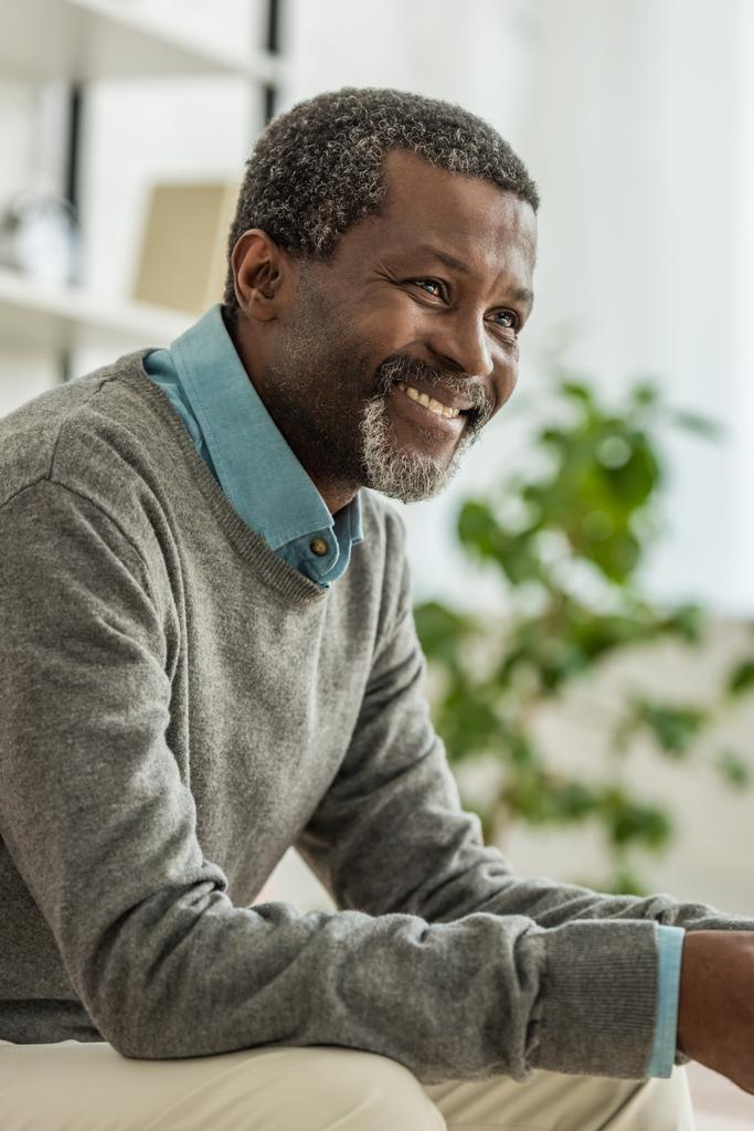 fröhlicher afrikanisch-amerikanischer Mann im grauen Pullover lächelt beim Wegschauen - Foto, Bild