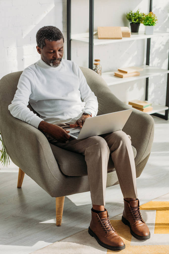 stylish, senior african american man sitting in armchair and using laptop - Photo, Image