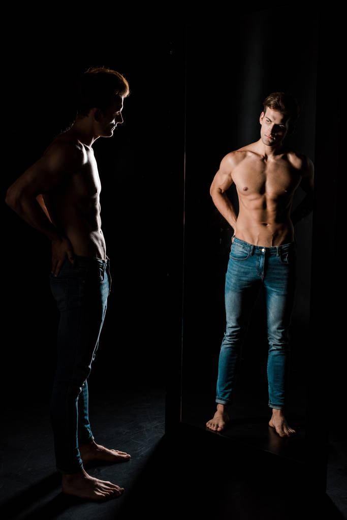красивий без сорочки чоловік позує перед дзеркалом у темній кімнаті
 - Фото, зображення