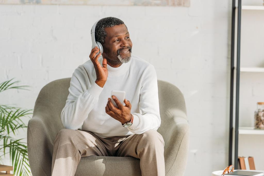 hombre afroamericano elegante sentado en sillón y escuchando música en auriculares
 - Foto, imagen