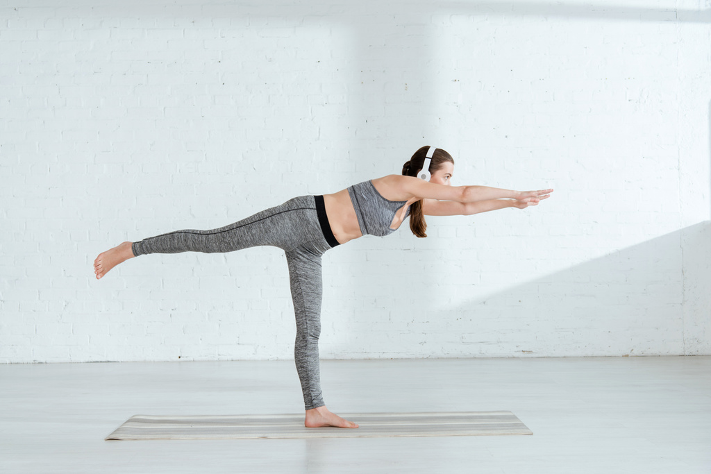 giovane donna in cuffia praticare yoga in posa guerriero III
 - Foto, immagini