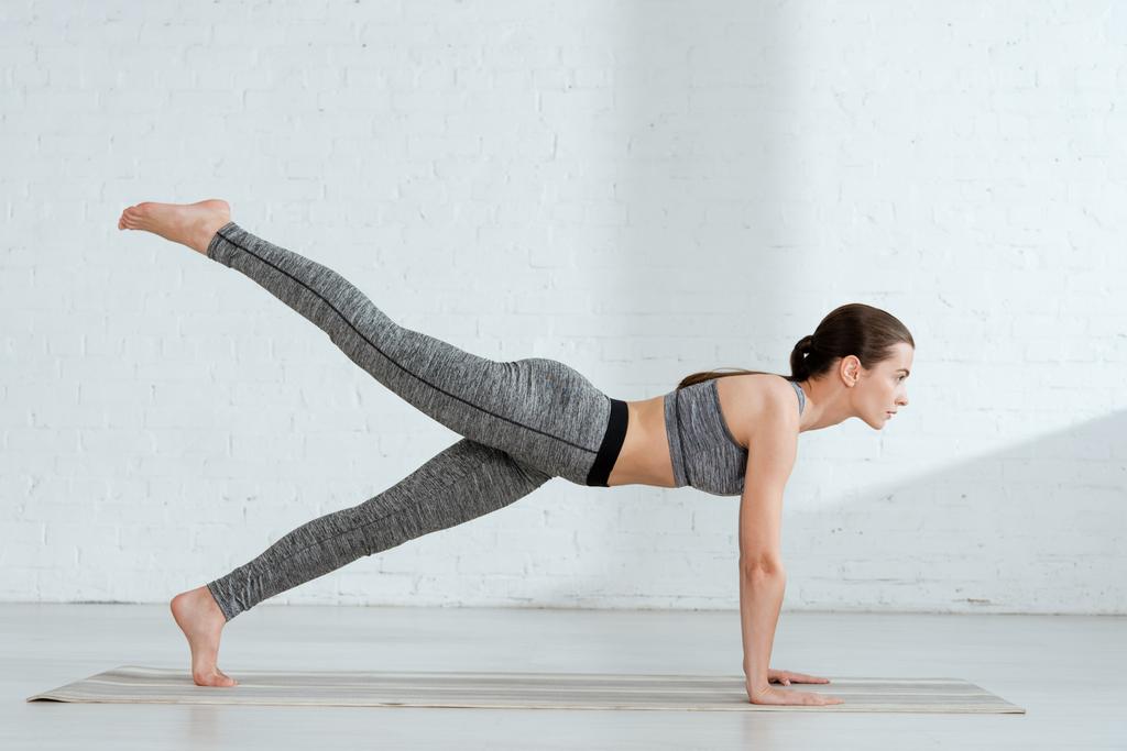 jovem mulher em sportswear praticando ioga em uma postura de prancha de perna
  - Foto, Imagem