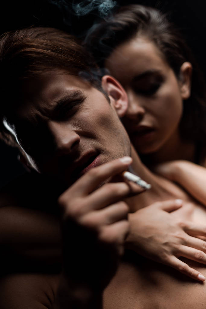 όμορφη γυναίκα που αγκαλιάζει τον άντρα που καπνίζει, απομονωμένη σε μαύρο - Φωτογραφία, εικόνα