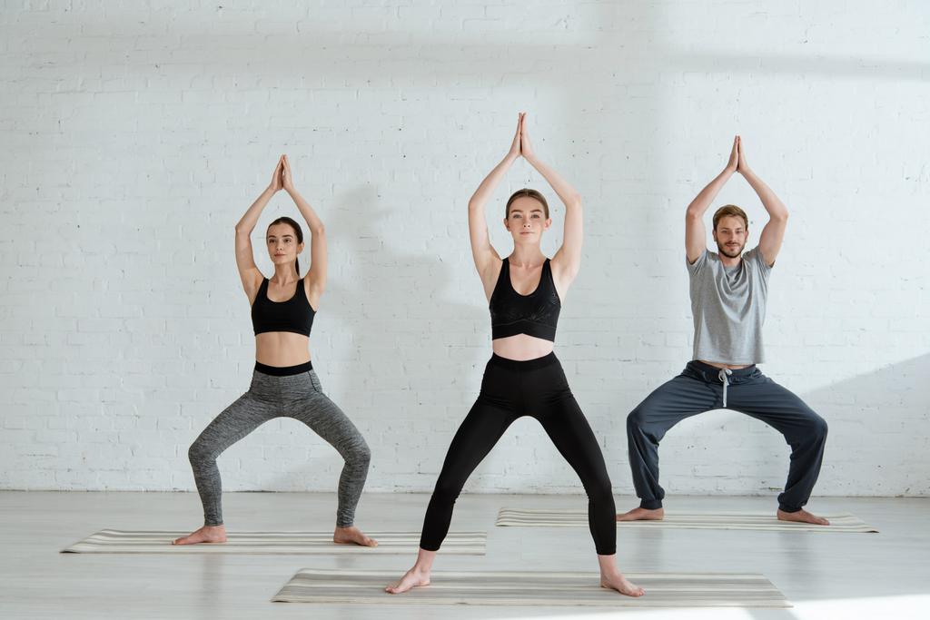 junge Männer und Frauen praktizieren Yoga in Göttin-Pose mit erhobenen Gebetshänden - Foto, Bild