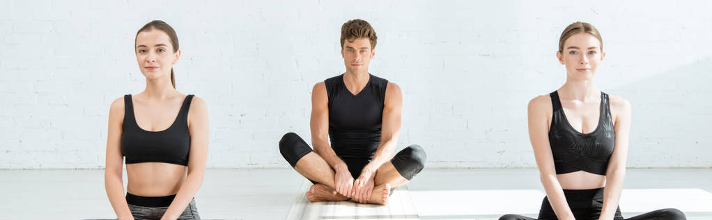 plano panorámico de mujeres jóvenes y hombres practicando yoga en pose de medio loto
 - Foto, imagen