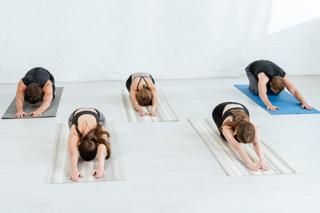 pięciu młodych ludzi ćwiczących jogę w rozszerzonych dziecięcych pozach - Zdjęcie, obraz