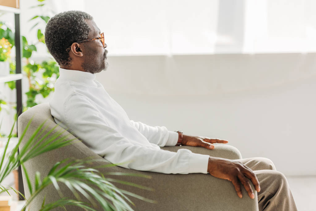 idős, stílusos afro-amerikai férfi ül karosszékben, és félrenéz - Fotó, kép