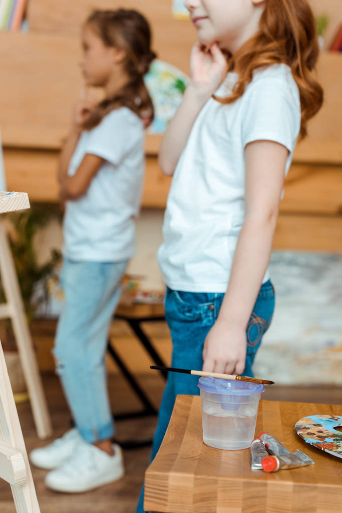 Ahşap masanın yanında duran ve elinde guaj boyası olan çocukların kırpılmış görüntüsü.  - Fotoğraf, Görsel