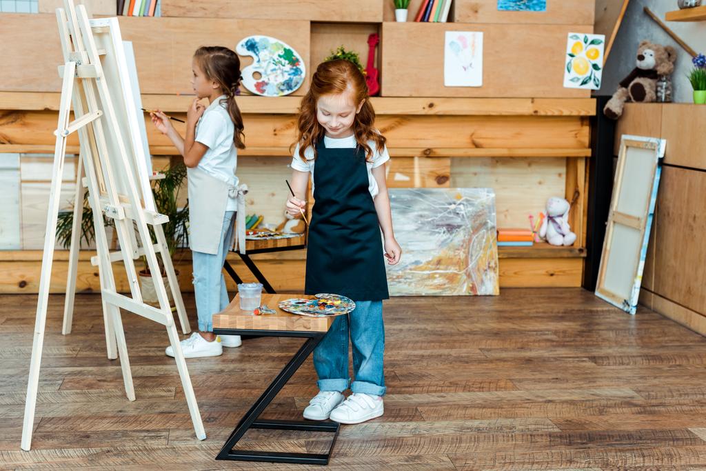 lindo pelirrojo niño sosteniendo pincel cerca colorido gouache pinturas y niño
  - Foto, Imagen