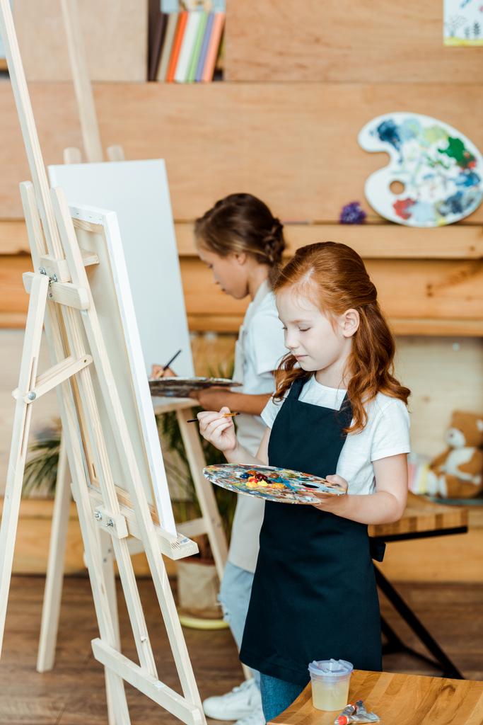 Niedliche Kinder mit Palette und Malerei in der Kunstschule  - Foto, Bild