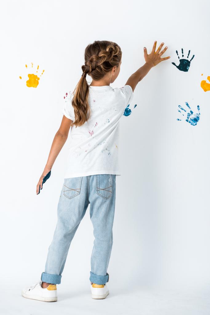 Вид сзади ребенка в джинсах, положившего руку рядом с принтами на белом
  - Фото, изображение