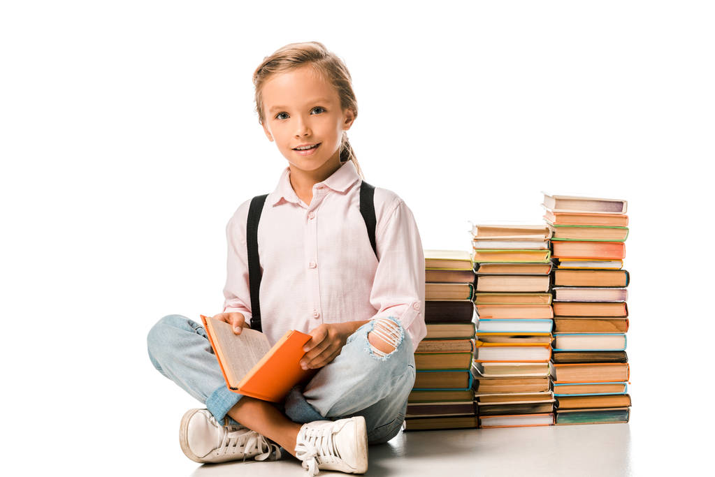 glückliches Kind sitzt mit überkreuzten Beinen in der Nähe von Büchern auf weiß  - Foto, Bild