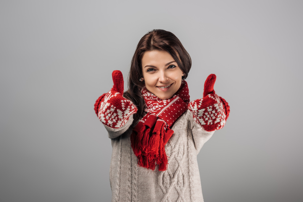 gelukkig vrouw in rood handschoenen en sjaal tonen duimen omhoog geïsoleerd op grijs  - Foto, afbeelding