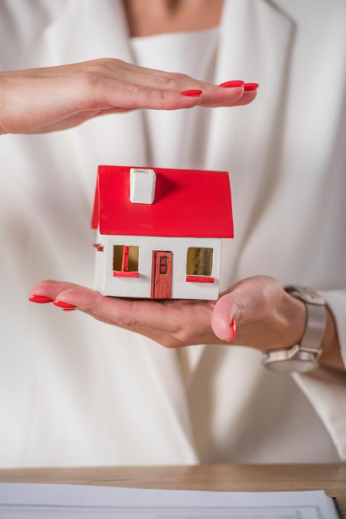 partial view of businesswoman holding and covering house model with hand  - Photo, Image