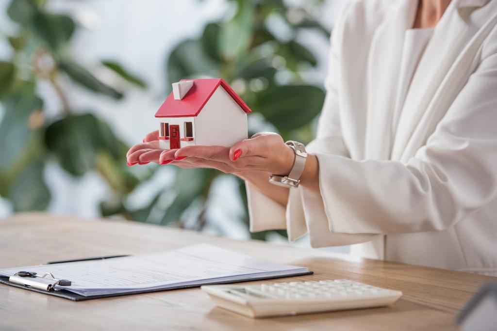 partial view of businesswoman holding house model near clipboard and calculator - Photo, Image