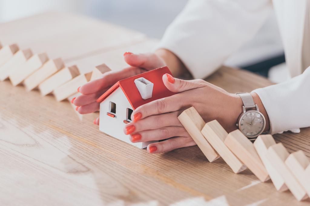 bijgesneden weergave van de risicomanager die huismodel beschermt tegen vallende houten blokken met handen - Foto, afbeelding