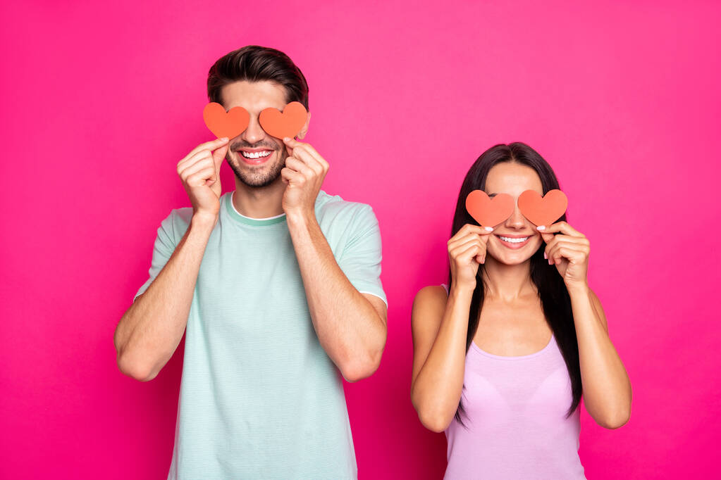 Фото удивительного парня и леди, держащих маленькие бумажные сердечки в руках, скрывающие глаза, приглашающие друг друга на студенческий бал носить повседневную одежду изолированный розовый цвет фона
 - Фото, изображение