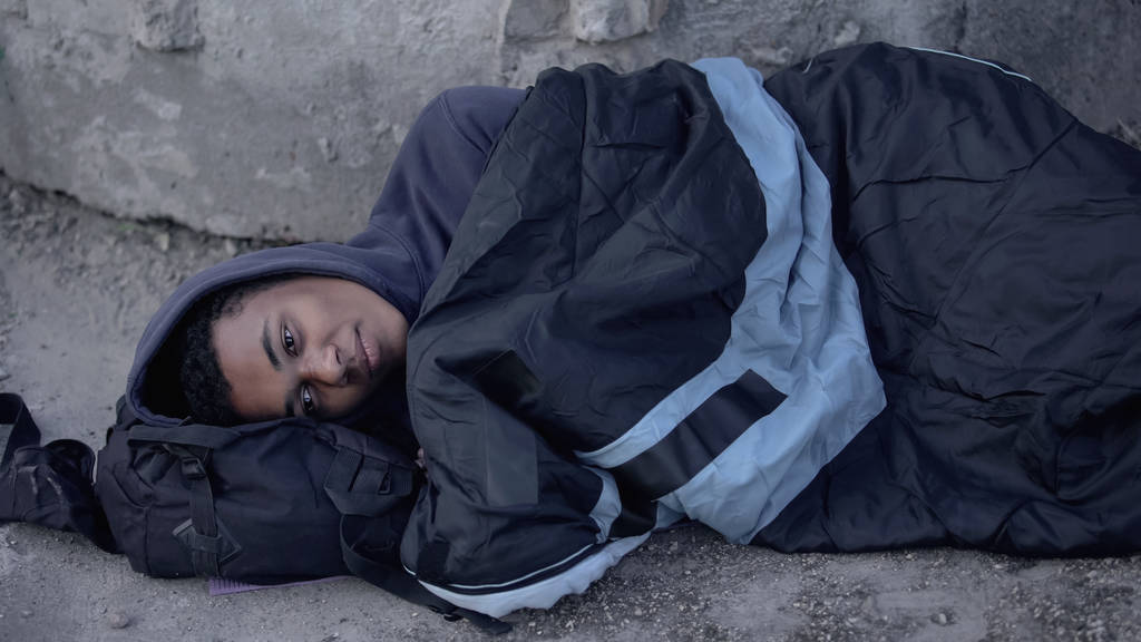 Відчайдушний чорний чоловік, що лежить на вулиці, вкритий спальним мішком, безнадійність бідності
 - Фото, зображення