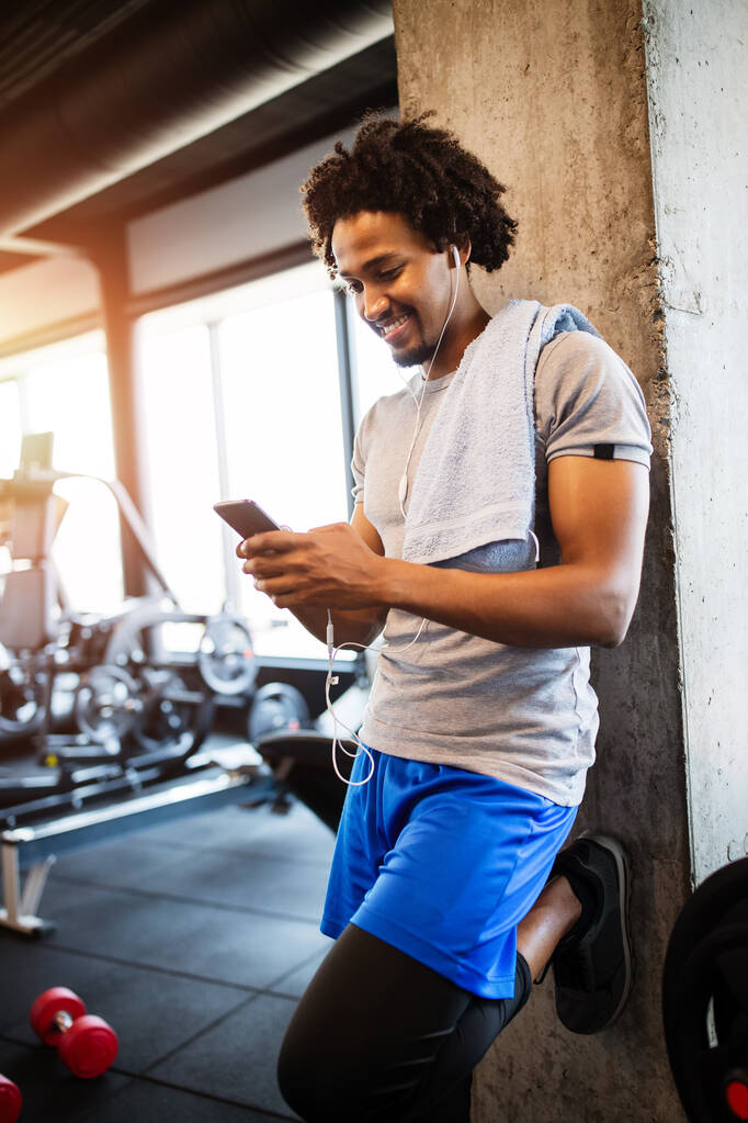 młody fit człowiek za pomocą telefonu podczas wykonywania przerwa w siłowni. - Zdjęcie, obraz