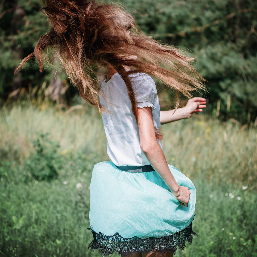 Etekli ve beyaz bluzlu genç bir kız atlıyor, açık havada uzun sarı saçlarını sallıyor, moda tonunda. - Fotoğraf, Görsel