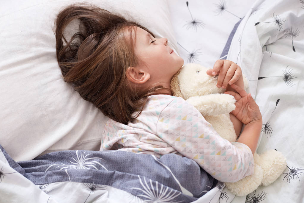 Roztomilá holčička ležící v posteli, usínající po celodenním hraní, ležící na bílém polštáři pod přikrývkou se zavřenýma očima, okouzlující dítě nosí pyžamo, holčička odpočívající ve svém pokoji. Dětský koncept - Fotografie, Obrázek