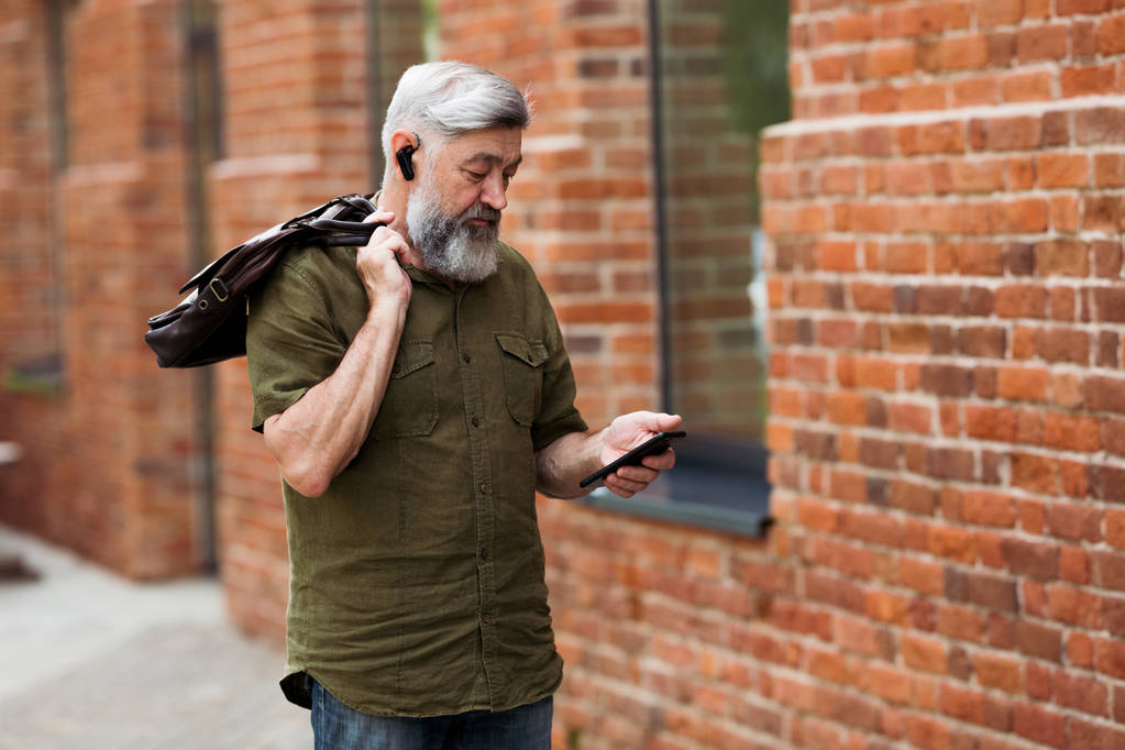 Gray-haired zakenman hipster in casual kleding staan in de steeg van het business center en belt een bericht op uw mobiele telefoon - Foto, afbeelding
