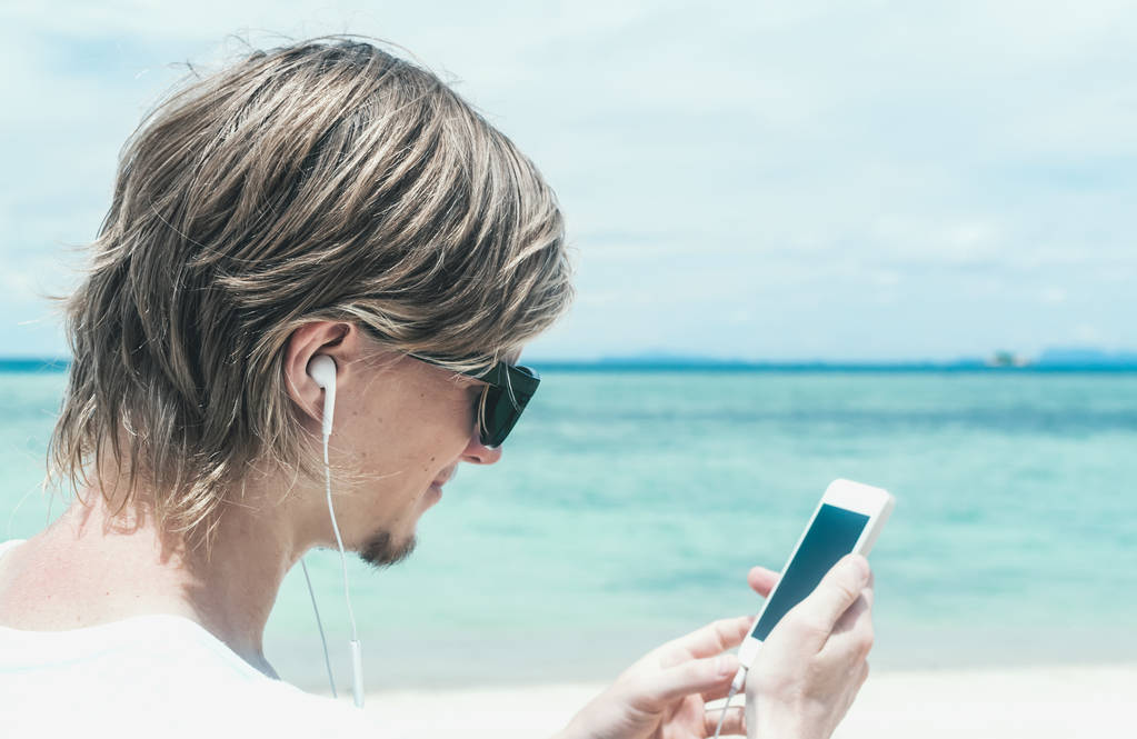 Vista laterale di un giovane uomo con le cuffie che ascolta musica sullo sfondo del mare
 - Foto, immagini