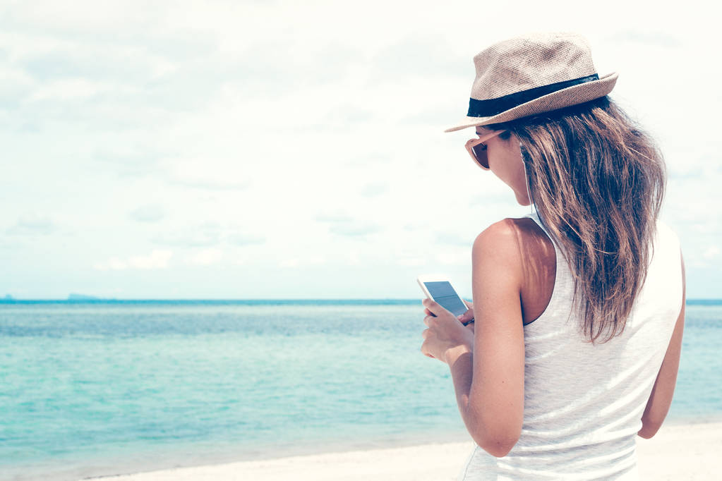 junge Frau zu Fuß auf schöne Bucht mit Telefon und Kopfhörer für die Kommunikation mit Freunden und Musik hören - Foto, Bild